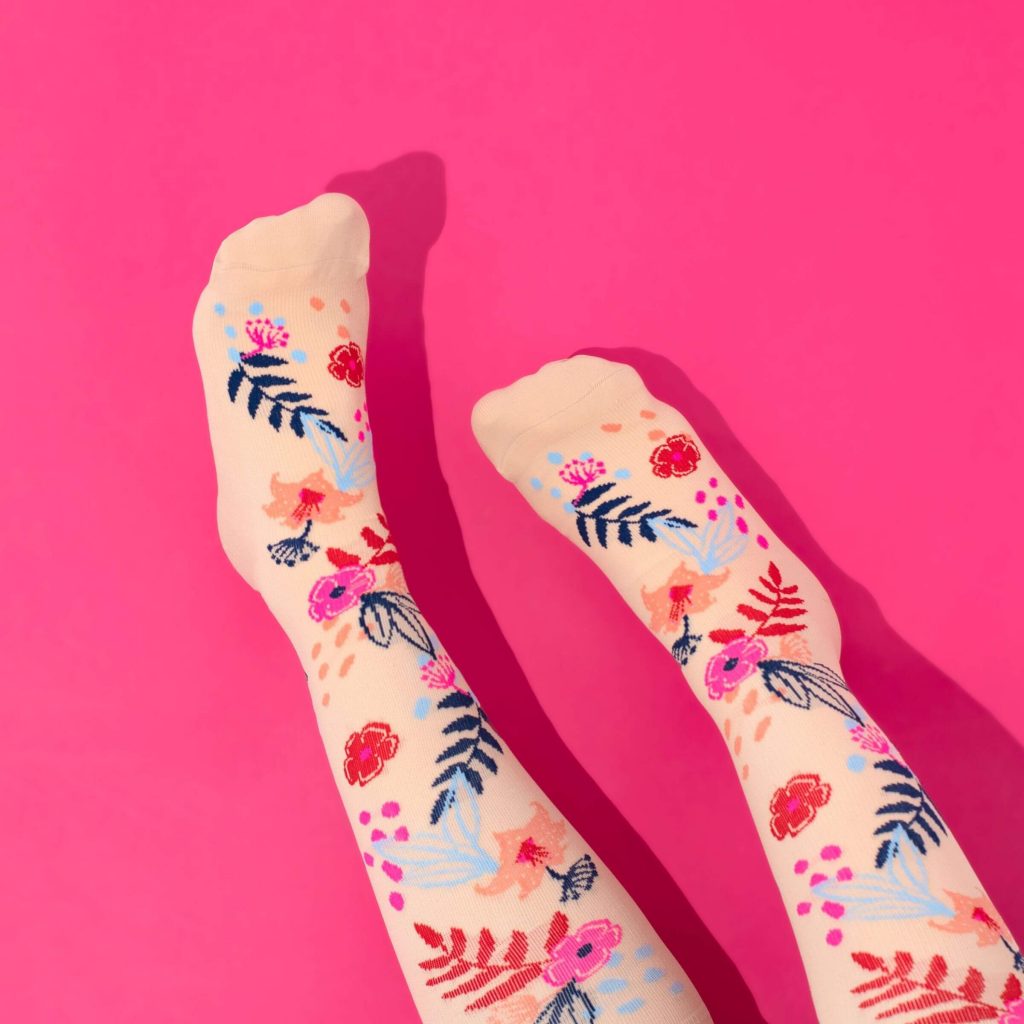 Peach coloured floral compression socks on a dark pink background